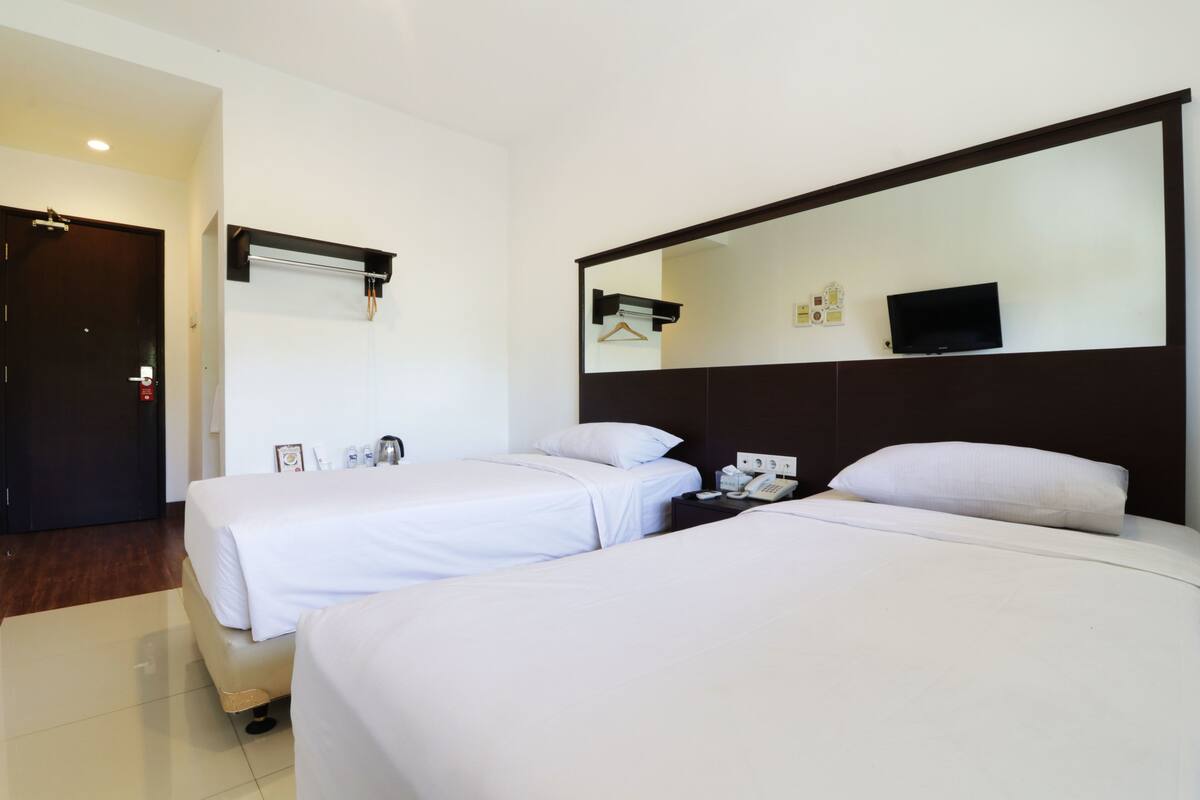 A hotel room with two beds, a TV, a bedside table, and a mirror.
