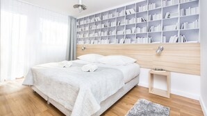 A modern bedroom with a large bed, a bedside table, a bookshelf, and a window with curtains. - Smart Hotel Garnizon (Gdansk)