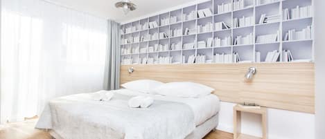 Un dormitorio moderno con una cama grande, una mesita de noche, una estantería y una ventana con cortinas.