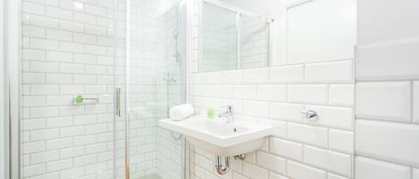 A modern bathroom with white subway tiles, a glass-enclosed shower, and a white sink with a mirror above it.