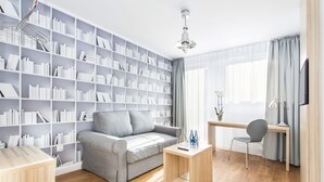 A modern living room with a grey sofa, a wooden coffee table, a bookshelf, and a desk with a chair. - Smart Hotel Garnizon (Gdansk)