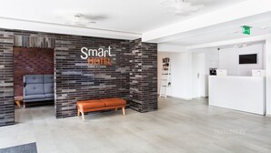 A reception area with a modern design, featuring a reception desk, a seating area with a bench, and a wall with a brick pattern. - Smart Hotel Garnizon (Gdansk)