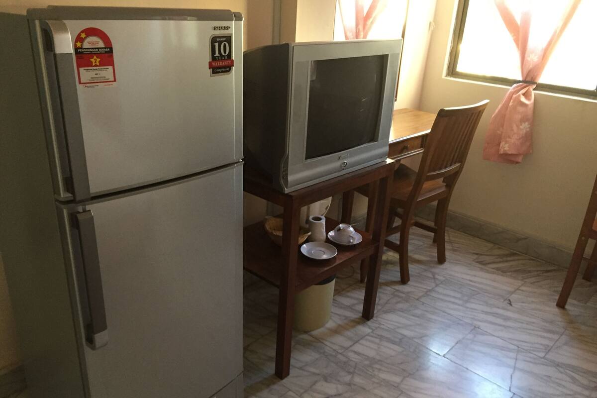 Una cocina compacta con refrigerador, microondas y televisor sobre una mesa de madera.
