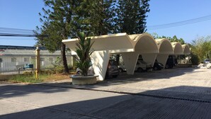 A parking area with multiple cars, a concrete planter with a palm tree, and a white fence with a utility box. - Seapark Condotel (Kota Kinabalu)