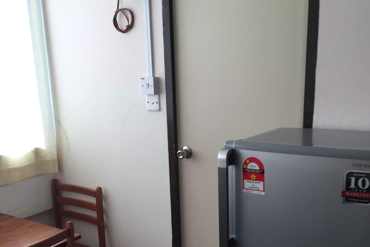 Cocina compacta con refrigerador, una mesa de madera y una silla. Se ve un enchufe y un dispositivo en la pared.