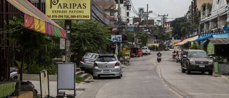 A street with parked cars and motorcycles, a sign for 'Paripas Express Parking', and buildings with visible power lines.