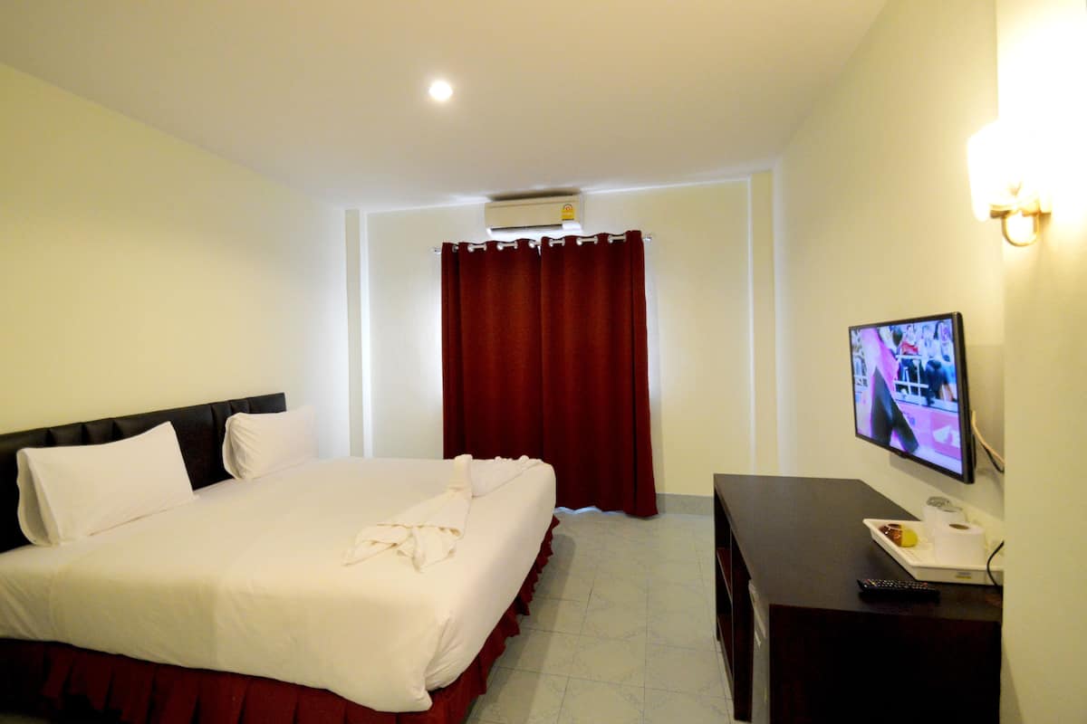 A hotel room with a bed, a TV, a desk, and a curtain.