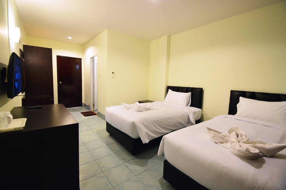 A hotel room with two beds, a desk, and a TV.