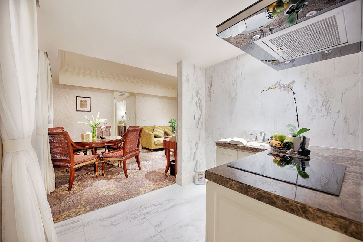 A modern kitchen with a marble countertop and a dining area with wooden furniture and a patterned rug.