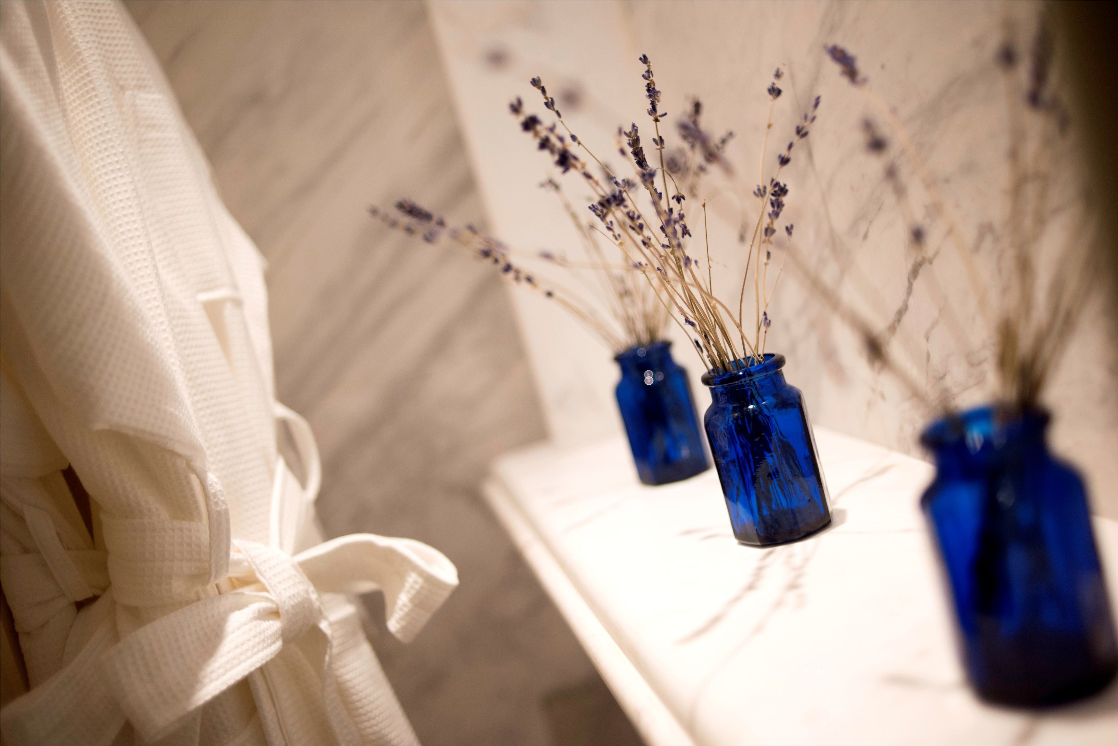 A bathroom with a white towel rack and three blue vases with dried lavender.