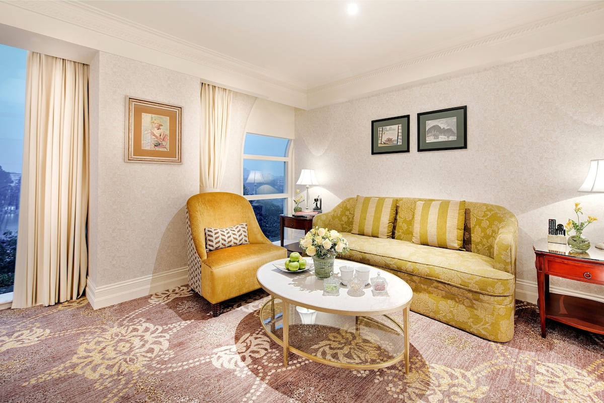 A hotel room with a sofa, armchair, coffee table, and a view of the city.