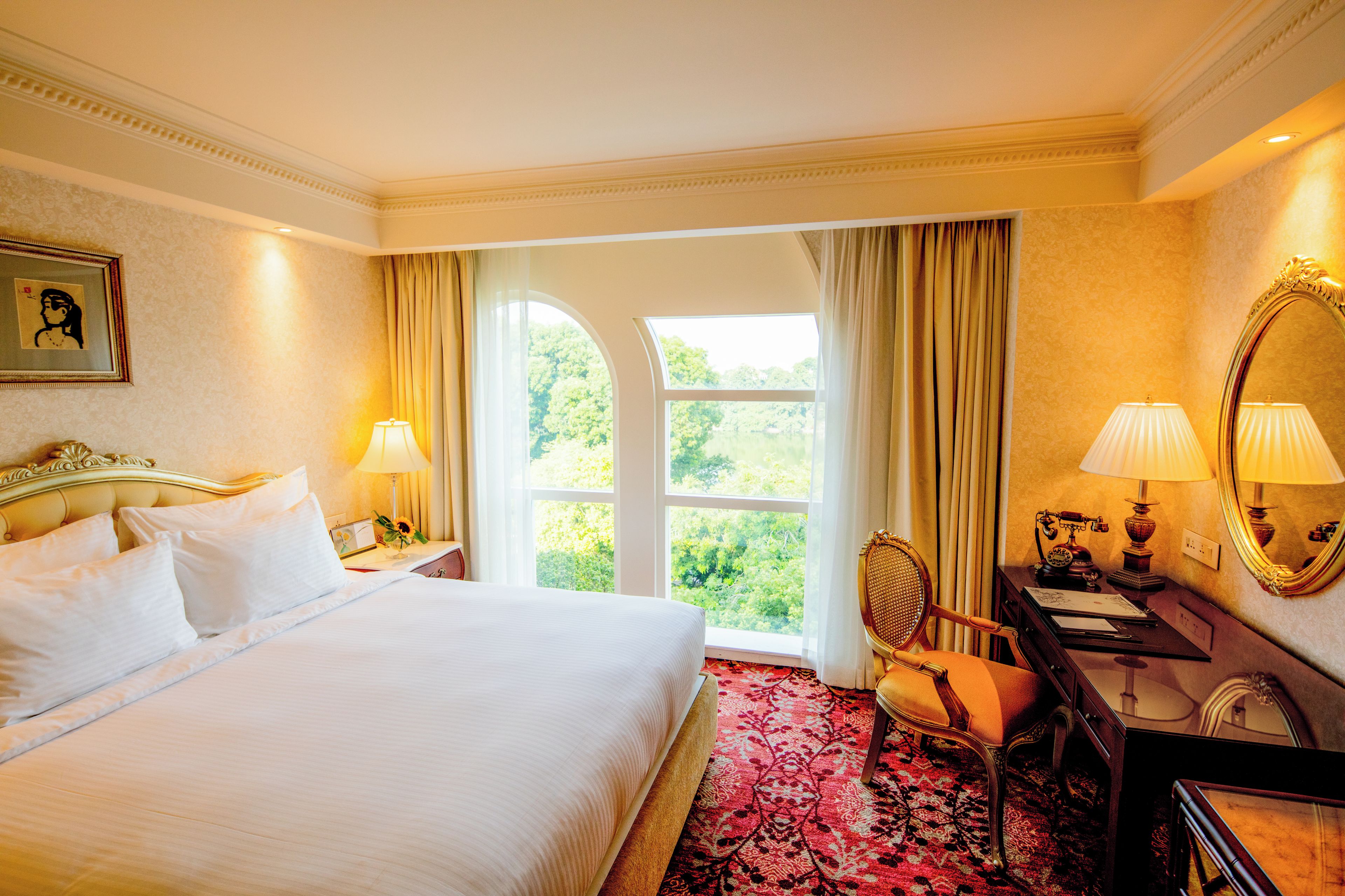 Habitación de hotel con una cama grande, un escritorio con teléfono, una silla y vistas a zonas verdes por la ventana.