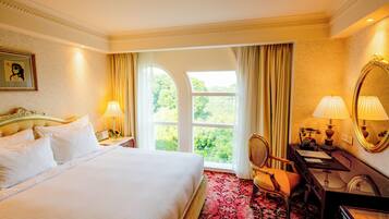 Habitación de hotel con una cama grande, un escritorio con teléfono, una silla y vistas a zonas verdes por la ventana.