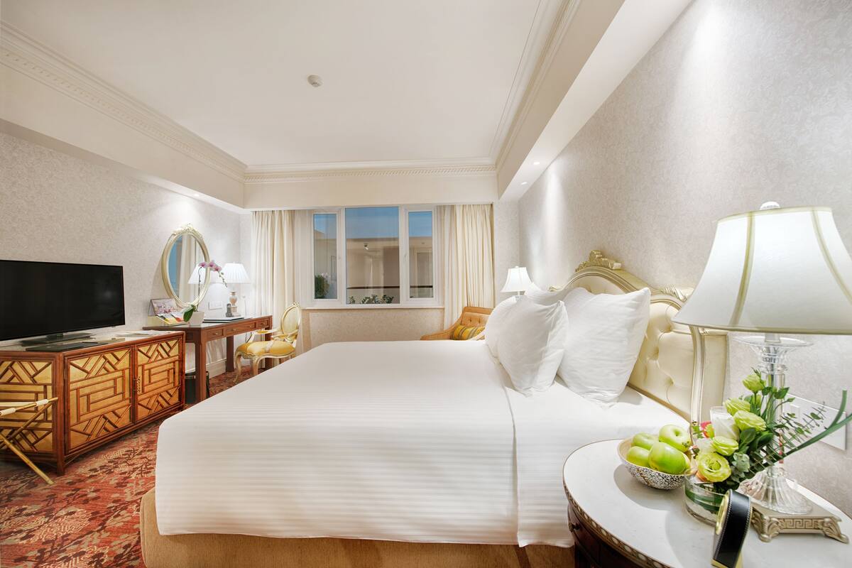 A hotel room with a large bed, a television, a desk with a mirror, and a window with curtains.