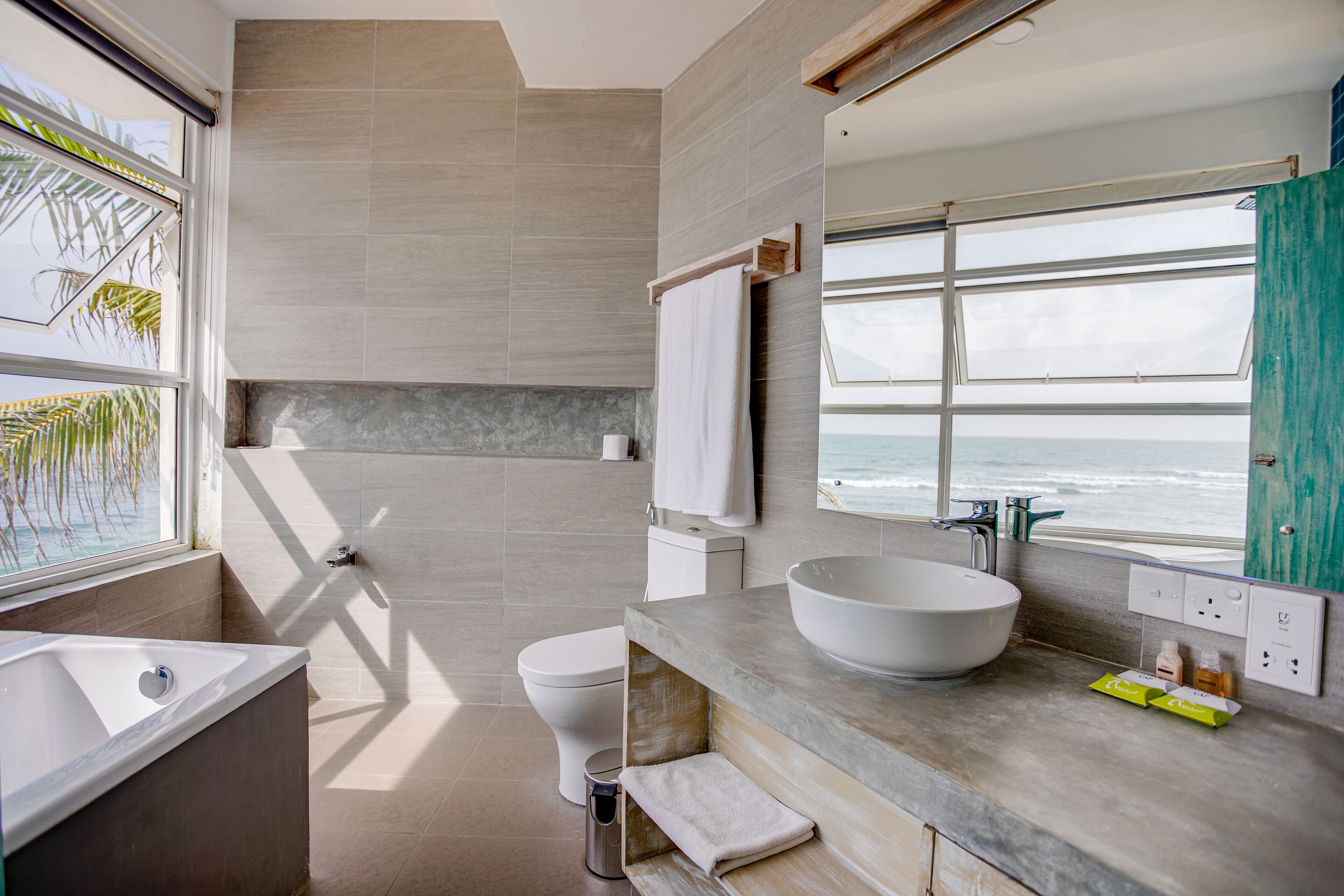 A modern bathroom with a large window, a bathtub, a toilet, and a sink.
