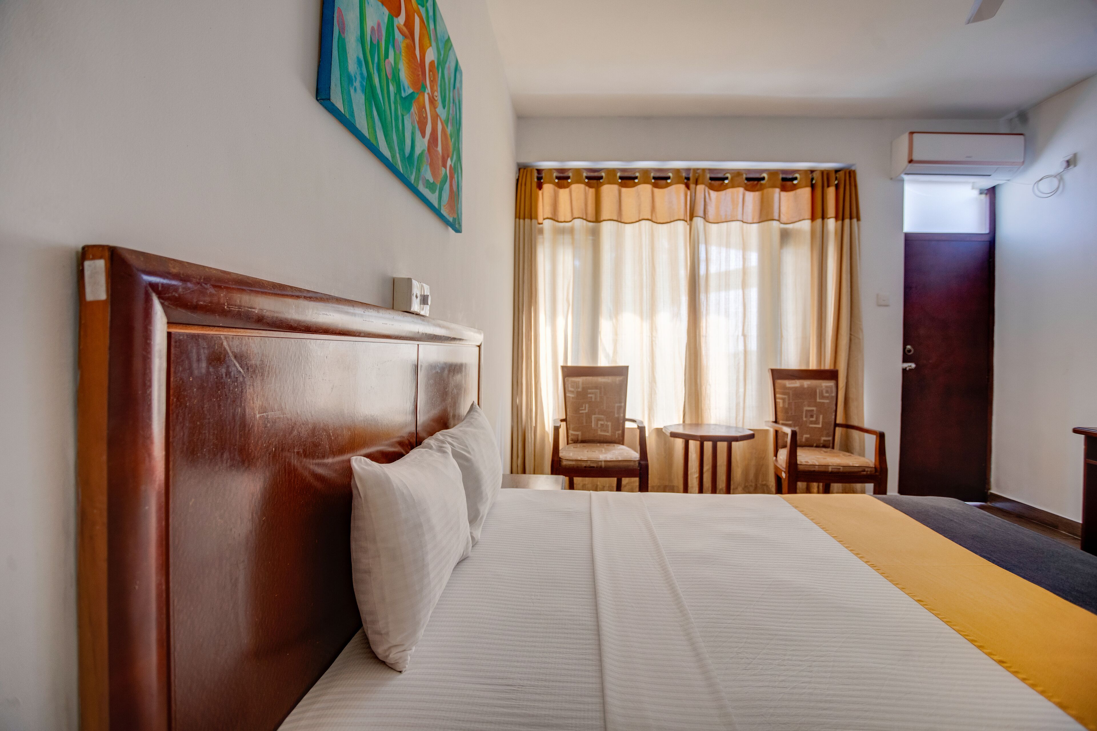 A hotel room with a large bed, two chairs, a small table, and a painting on the wall.