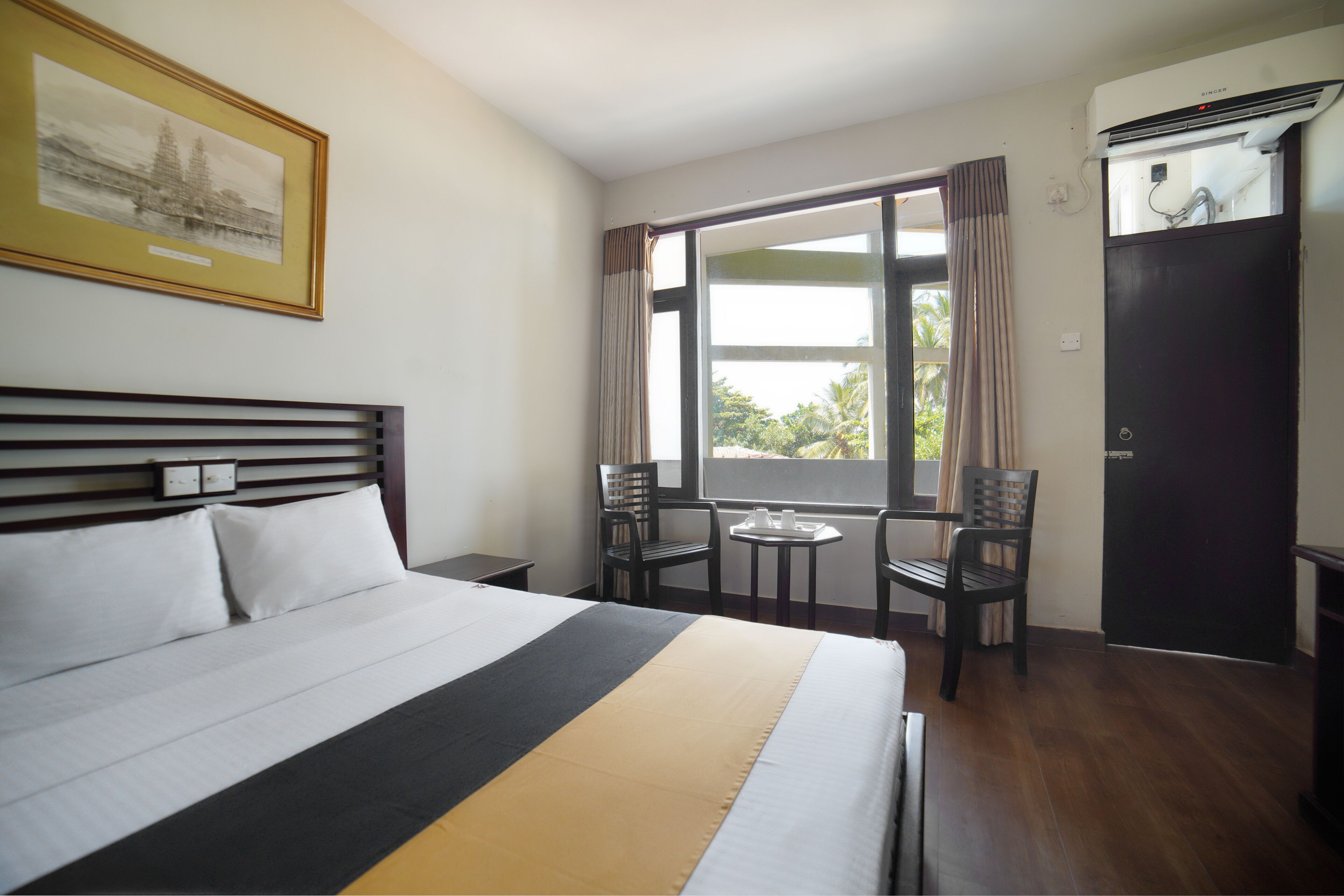 Una habitación de hotel con cama, escritorio, dos sillas, ventana con cortinas y aire acondicionado.