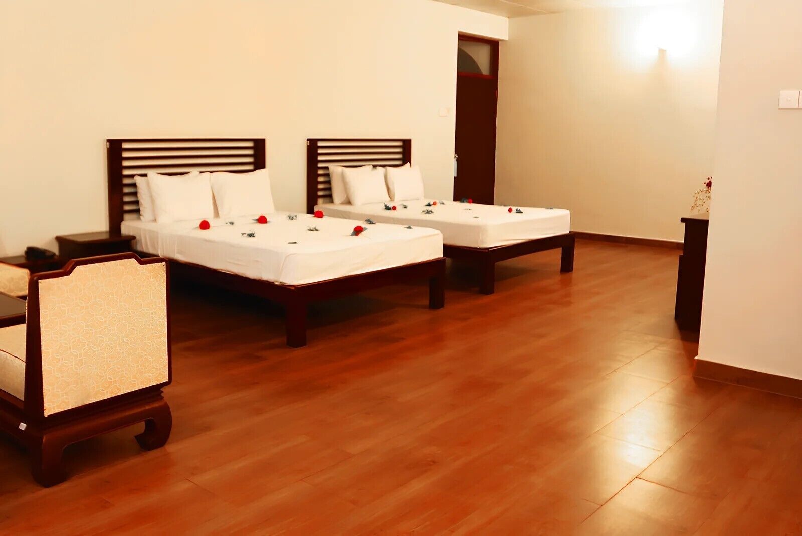A hotel room with two beds, wooden flooring, and a nightstand with a lamp.