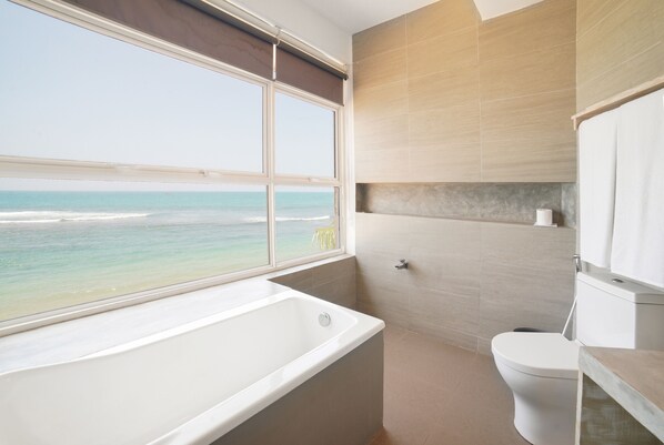 Un baño con bañera, inodoro y vista al océano.