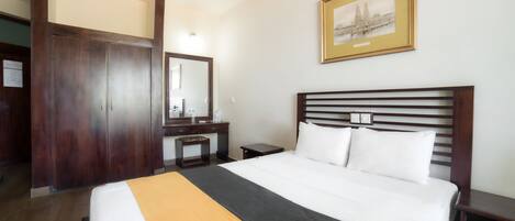 A hotel room with a large bed, wooden wardrobe, bedside table, and a framed picture on the wall.