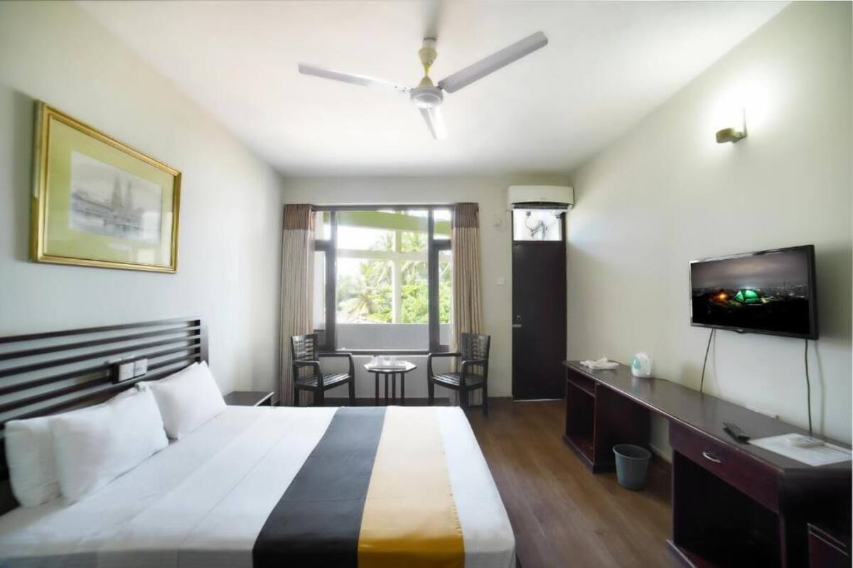 Une chambre d’hôtel équipée d’un lit, d’un bureau, d’une télévision, d’un ventilateur de plafond et d’une fenêtre avec des rideaux.