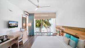 Habitación de hotel con cama, escritorio, silla, televisor y balcón con vista a palmeras y al mar.