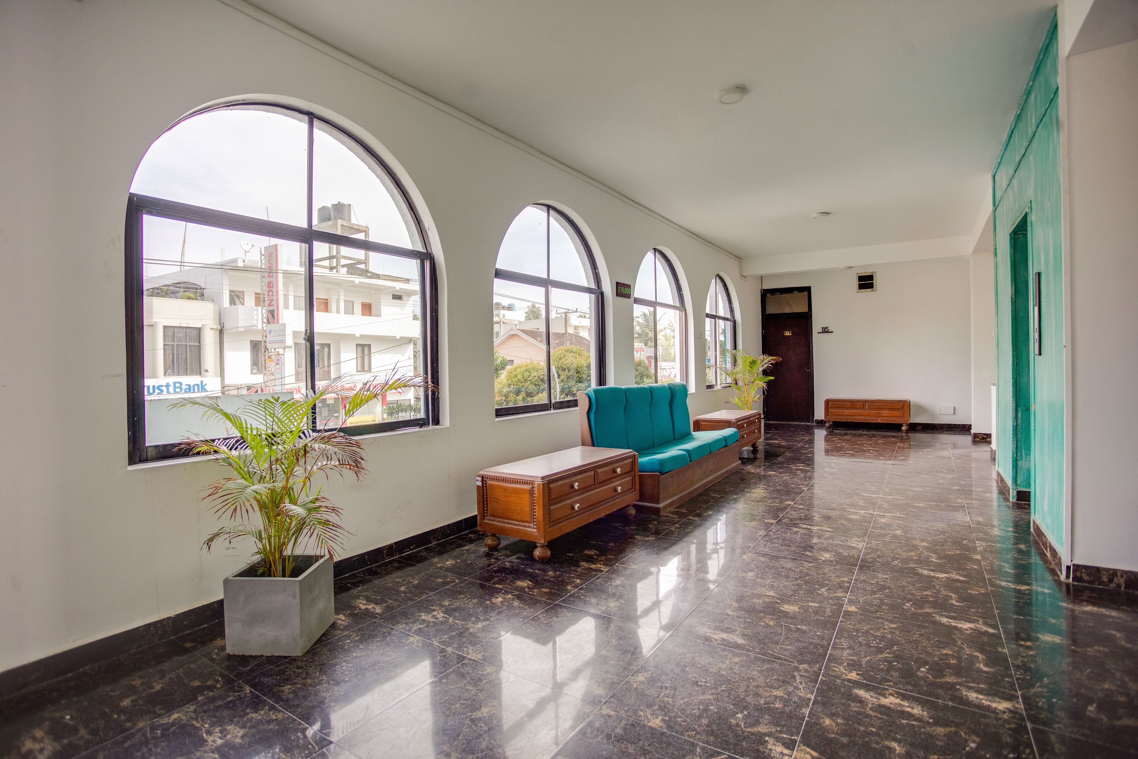 Un pasillo amplio con ventanas arqueadas grandes, un banco de madera y una planta en maceta.