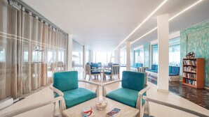 Una biblioteca moderna con sillas color turquesa, una mesa de madera con libros y un separador de vidrio.