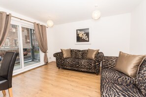 A modern living room with a zebra-patterned sofa, a black leather chair, and a glass door leading to an outdoor area.