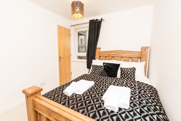 A neatly made bed with a geometric patterned bedspread, two pillows, and two folded towels.