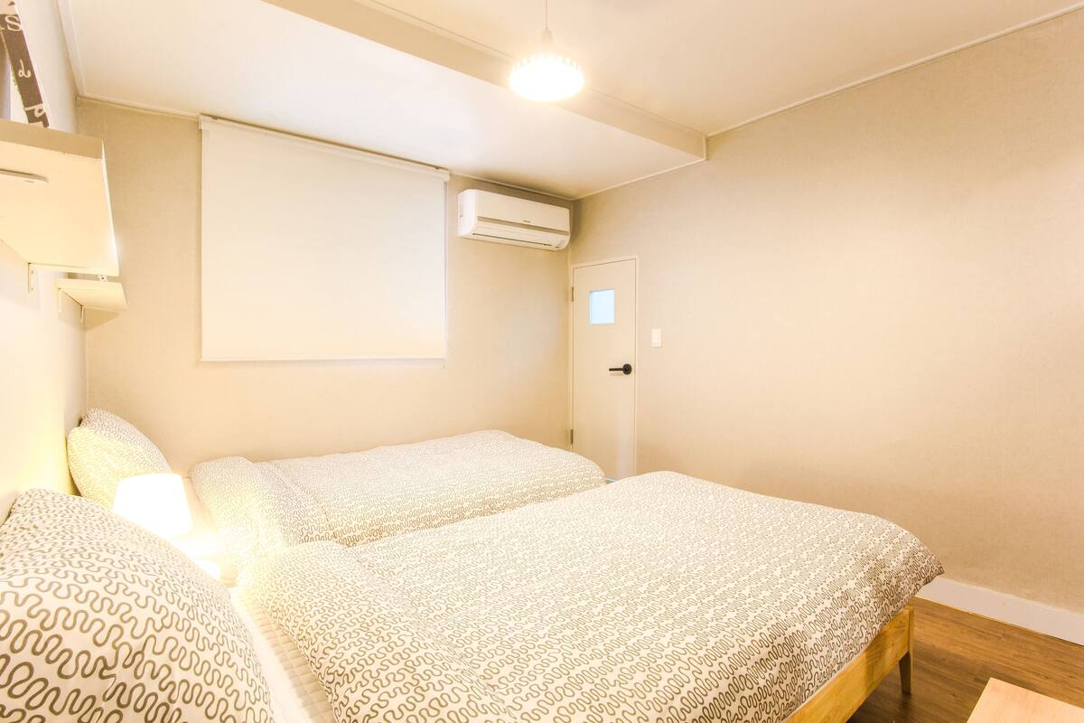 A bedroom with two beds, a ceiling light, an air conditioning unit, and a door.