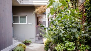 Un sendero estrecho bordeado por plantas en macetas y un edificio con el letrero "Vanilla Suite".