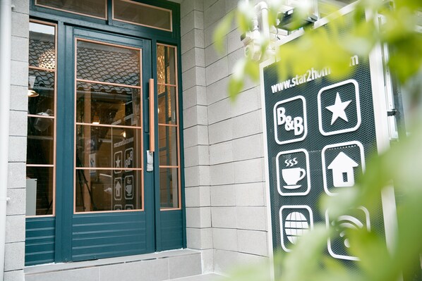 Entrada de un edificio con una puerta azul oscuro, un ventanal de vidrio y un cartel con varios iconos, incluyendo una estrella, una taza de café y el símbolo de Wi-Fi.