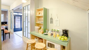 Cocina con mostrador verde, microondas y cafetera. Hay taburetes y una cesta de frutas.