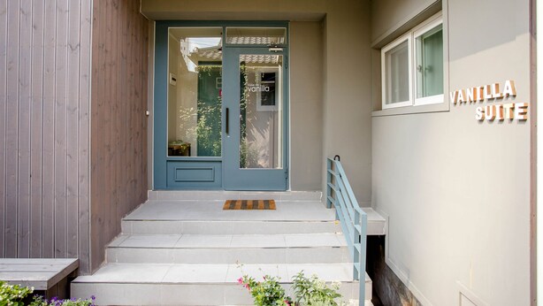 Entrada de un edificio con una puerta azul, una escalera y un cartel que dice 'VANILLA SUITE'.
