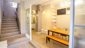 Un moderno vestíbulo de hotel con una escalera, suelo de madera, un mostrador de recepción y un comedor con mesa y bancos de madera.