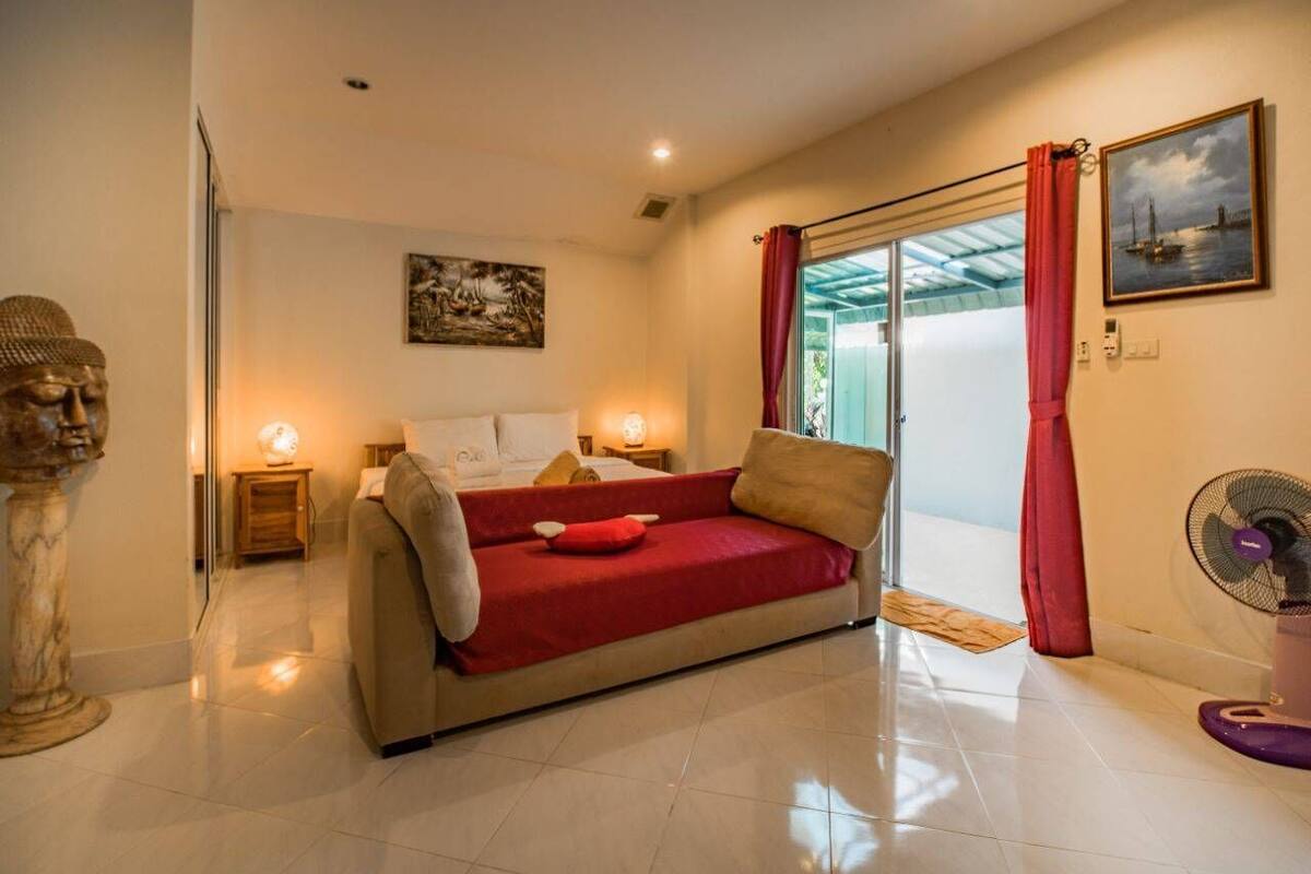 Quarto com cama, manta vermelha, ventoinha e janela com cortinas vermelhas.