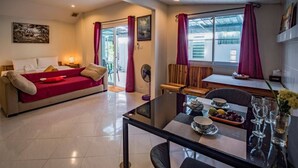 Una sala de estar moderna con un sofá rojo, una mesa de comedor de vidrio con platos y vasos, y vistas al exterior a través de amplias ventanas.
