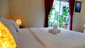 Una cama bien hecha con una toalla enrollada, una lámpara de noche y vistas al verdor del exterior.