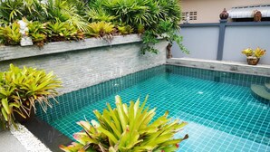 Una piscina con borde de azulejos, rodeada de plantas y un muro de piedra.