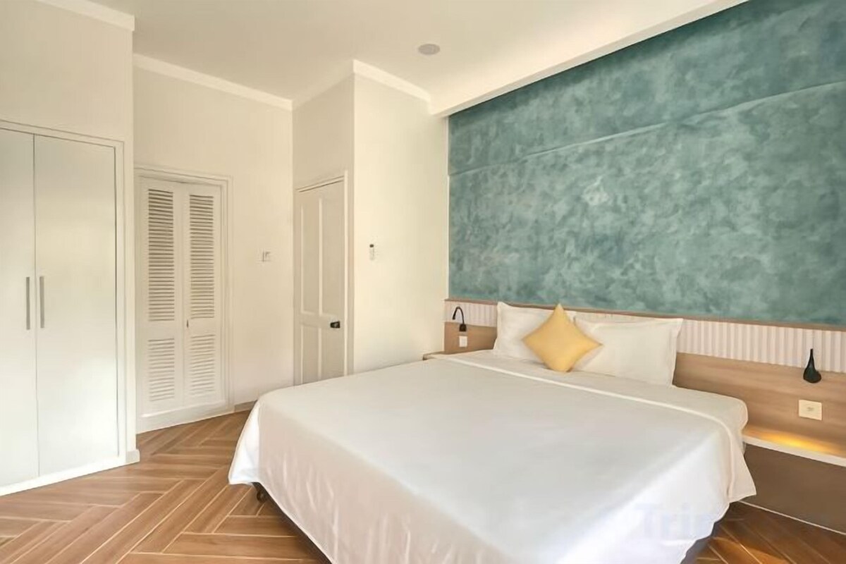 A hotel room with a large bed, a wardrobe, and a headboard with a textured design.