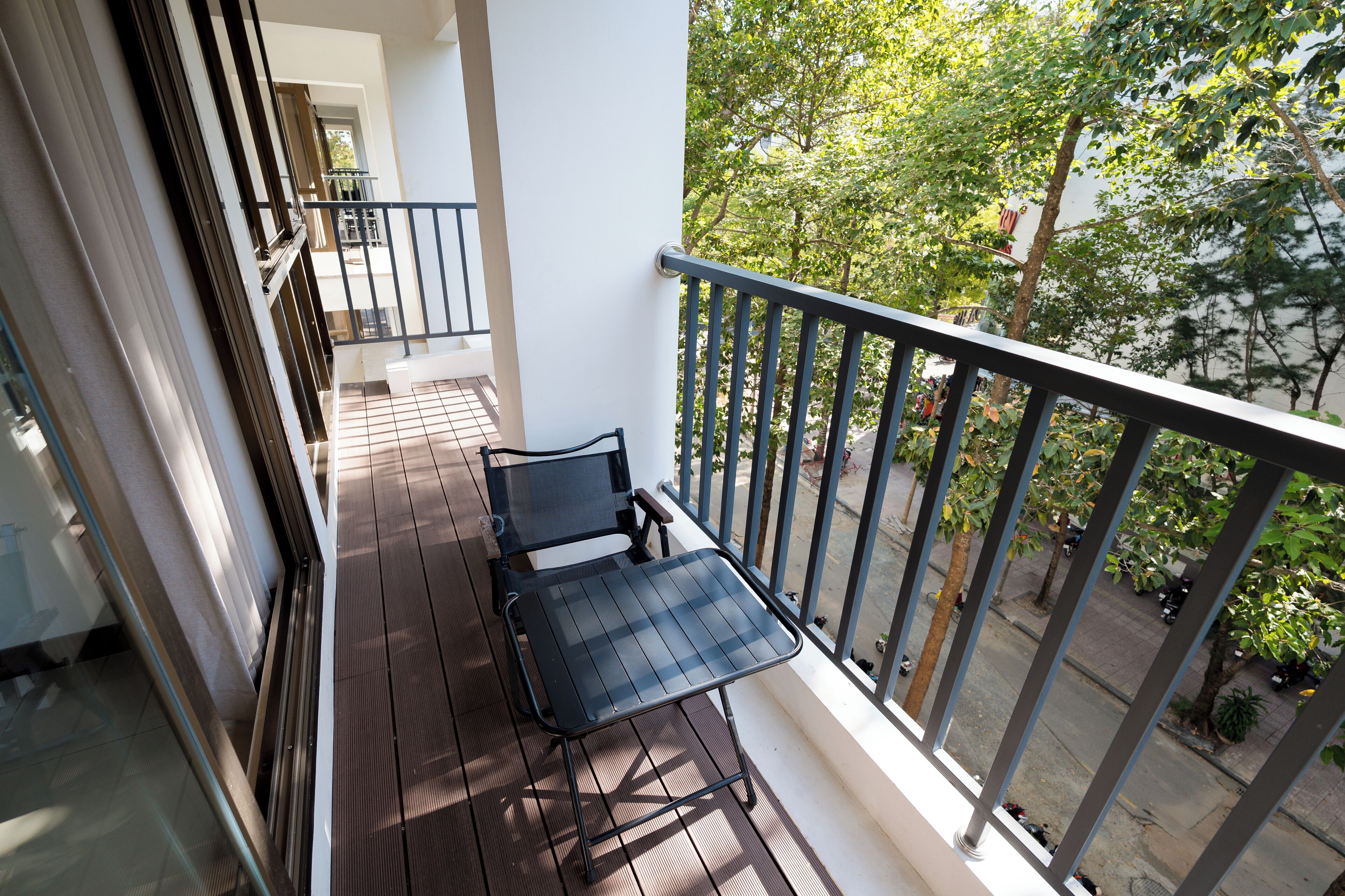 A balcony with a table and chairs, a railing, and a view of trees and a street.