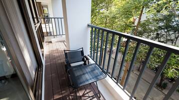 A balcony with a table and chairs, a railing, and a view of trees and a street.
