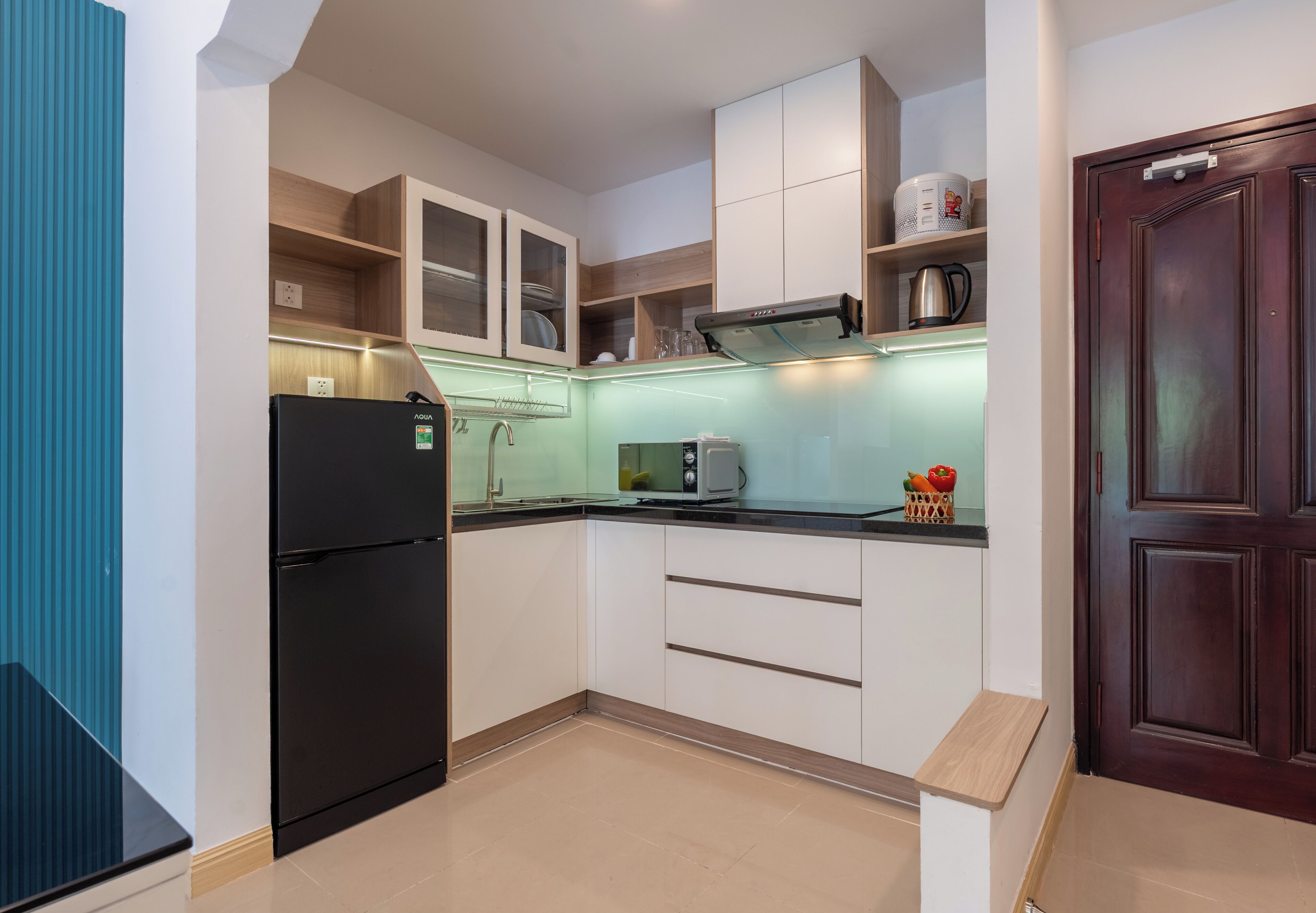 Une cuisine de taille réduite avec un réfrigérateur noir, un four à micro-ondes et un meuble en bois.