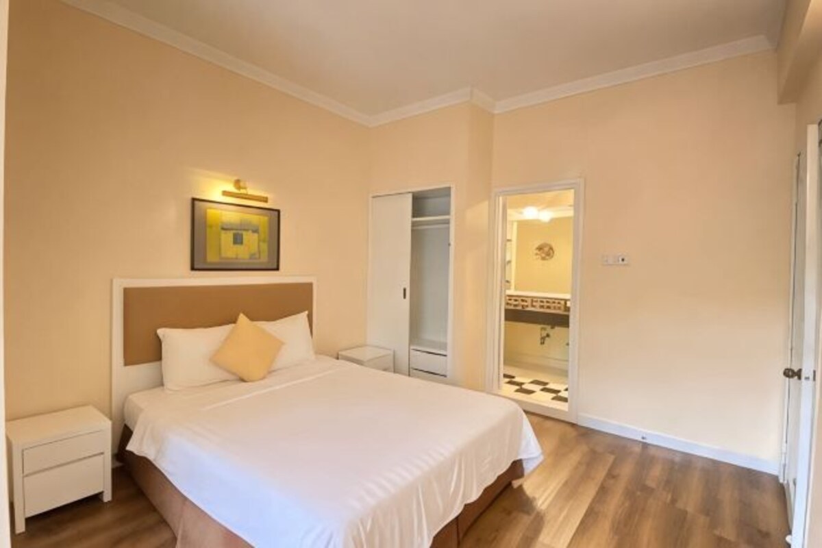 A bedroom with a bed, nightstands, a wardrobe, and a door leading to a bathroom.