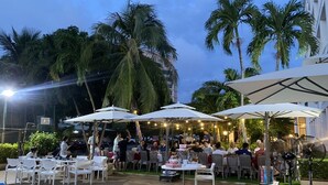 An outdoor dining area with tables and umbrellas, surrounded by palm trees and a pool. - Ocean Sunrise Vung Tau (Ho Chi Minh City)