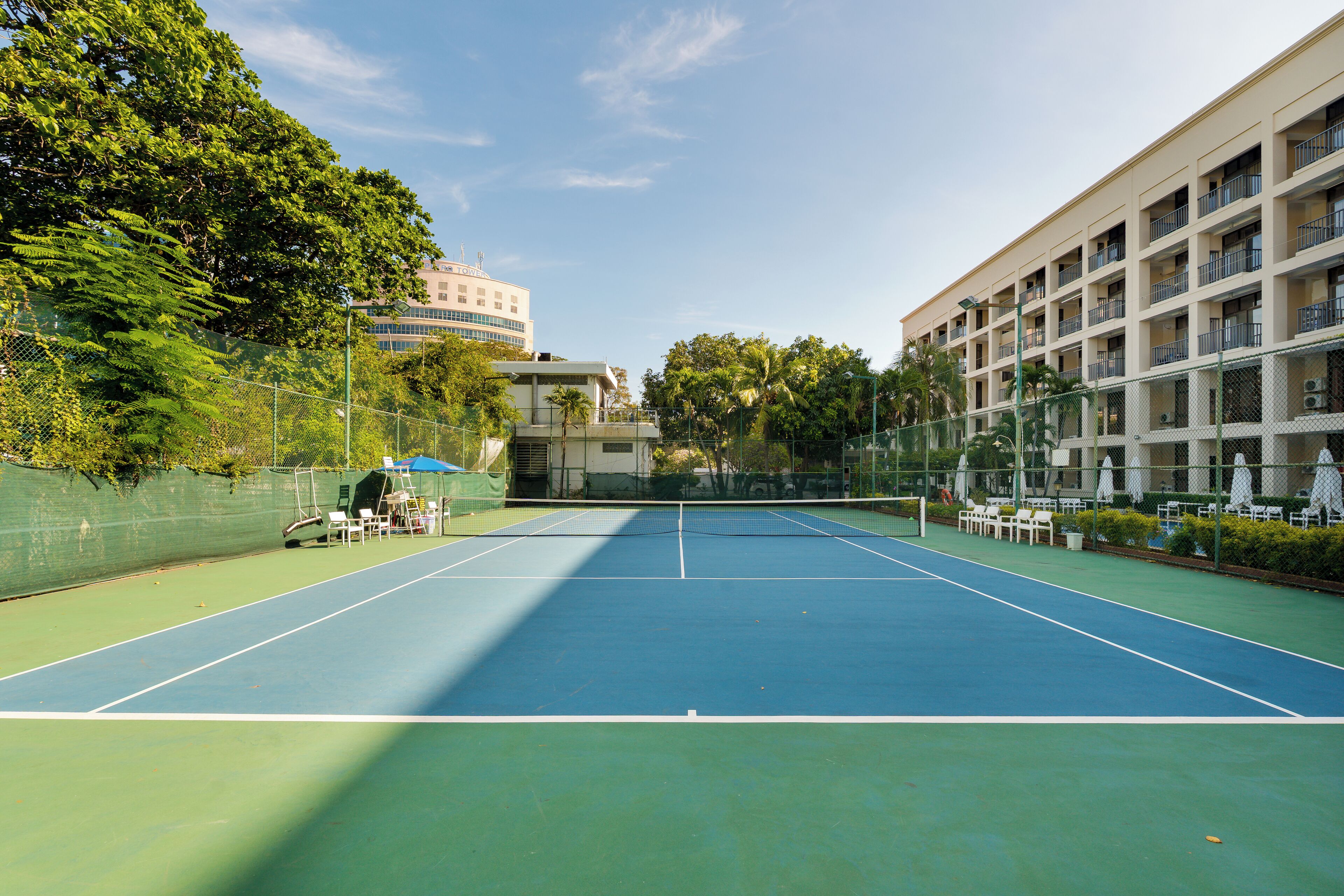 A tennis court with a net, surrounded by a fence, and adjacent to a building with multiple balconies.
