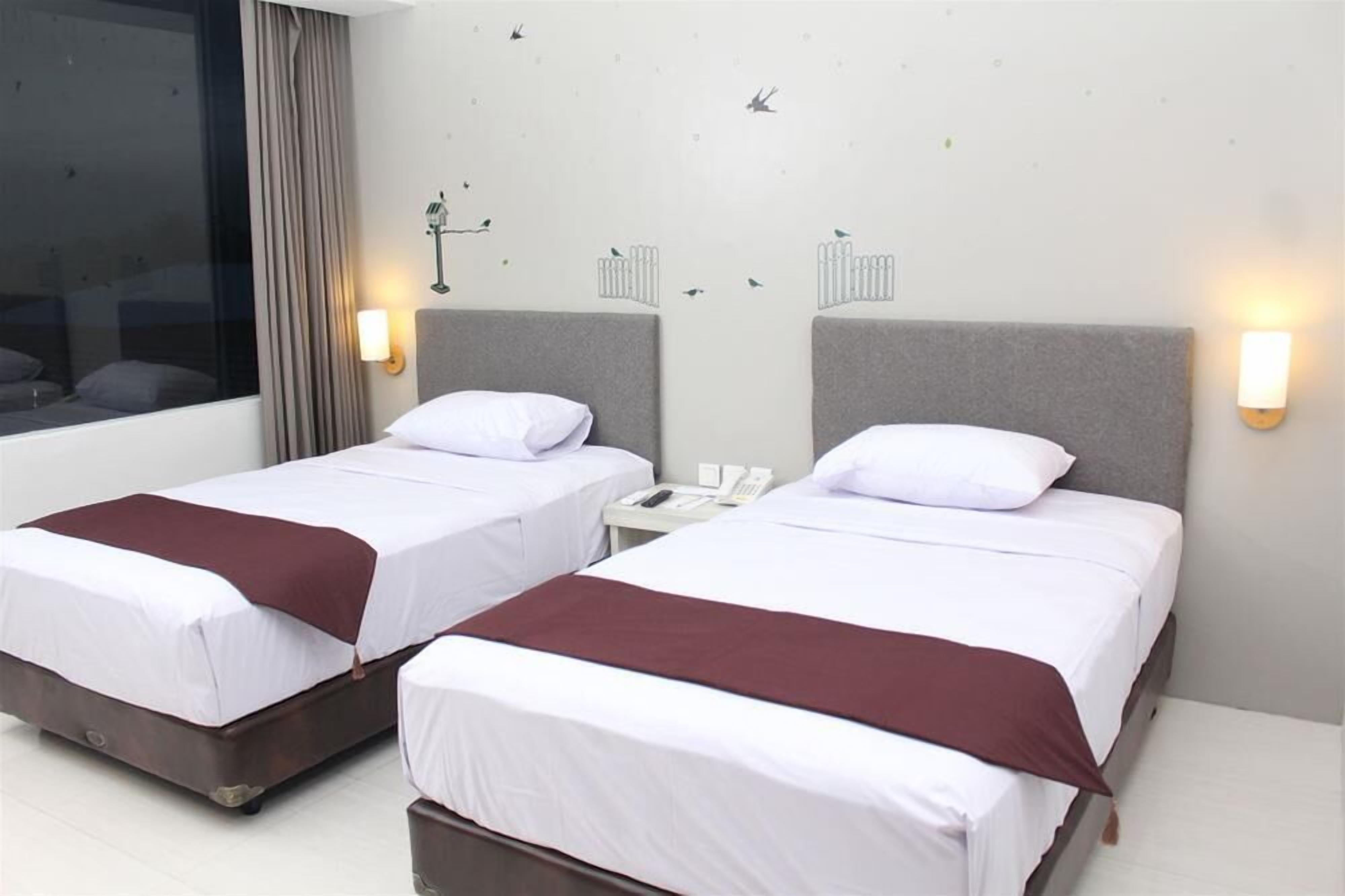 A hotel room with two single beds, a nightstand with a phone, and a window with curtains.