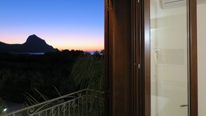 Varanda com vista para uma montanha e um corpo de água ao pôr do sol.