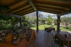 Un espace extérieur aménagé pour les repas, doté d’un toit abrité, d’une table de buffet proposant divers plats, et offrant une vue sur un paysage montagneux.